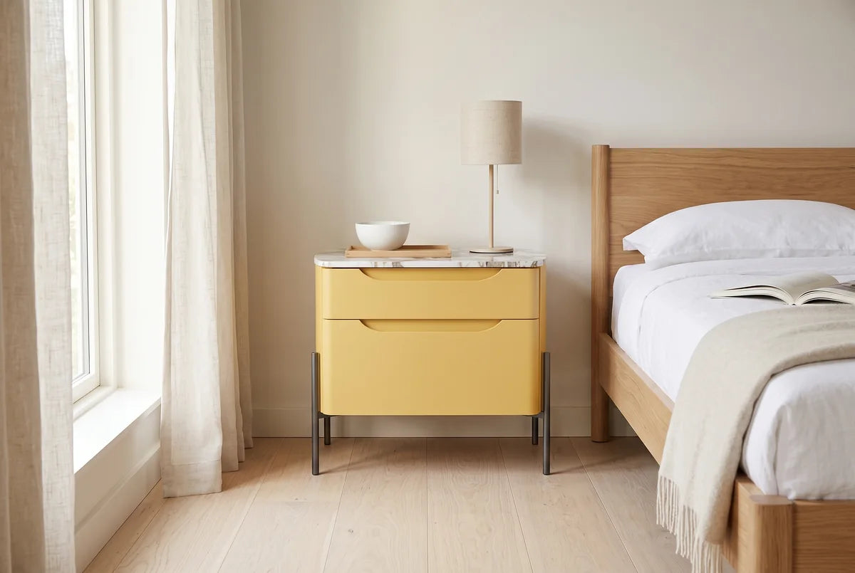 Ambra nachtkastje met 2 laden naast een bed in een lichte, warme slaapkamer (AI-sfeerbeeld)