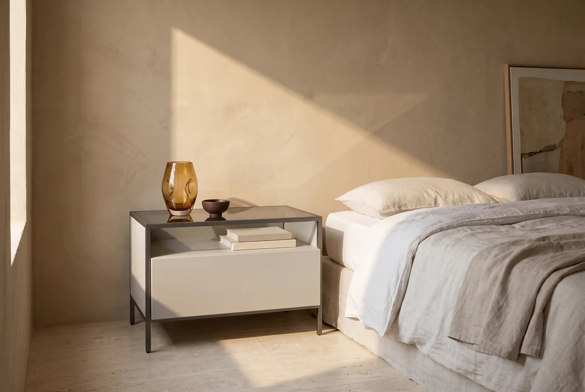Frame nachtkastje breed met 1 lade naast een bed in een lichte, warme slaapkamer (AI-sfeerbeeld)