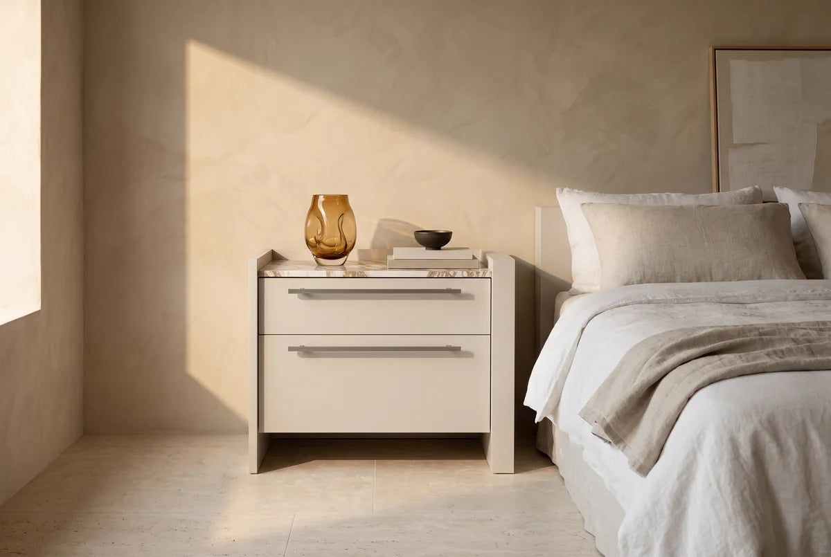 Carry nachtkastje met 2 laden, greep rechts naast een bed in een lichte, warme slaapkamer (AI-sfeerbeeld)