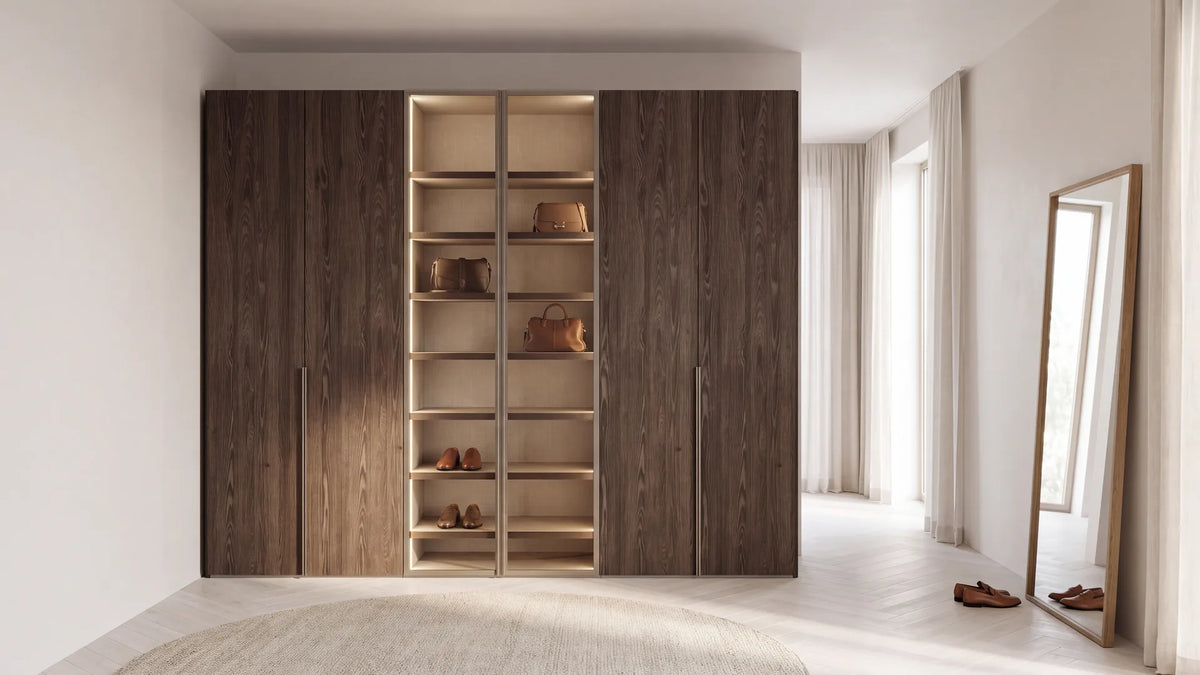 FOEHN-draaideurkast in Rovere Fiammato met twee glazen deuren in Bronzo en verlichte planken met tassen en schoenen, in een lichte kleedkamer (AI-sfeerbeeld)